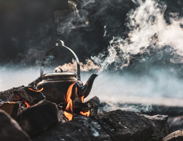 A close-up of a kettle boiling on a fire. There's smoke coming out from the kettle as well as from the fire.